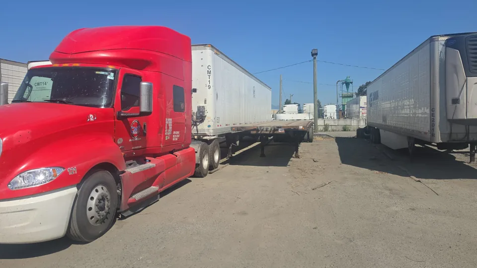 Red C M T Transport tractor parked beside a flatbed trailer in the fleet yard
